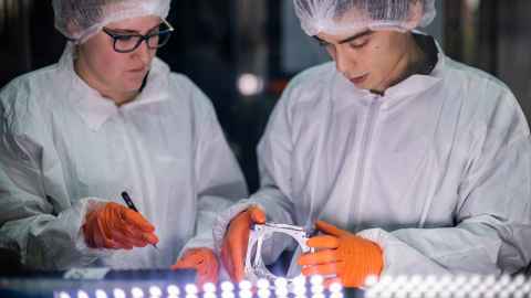 Two students examine a CubeSat in the APSS cleanroom